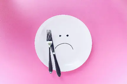 عکس مفهومی بشقاب خالی با چنگال در پس زمینه صورتی