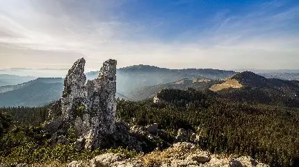 عکس کوهستان و صخره های رومانی با آسمان آبی و درختان