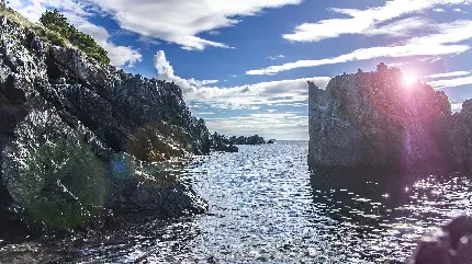 تصویرزمینه از صخره های خیس ، آسمان ابری و نور آفتاب