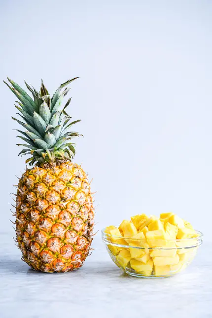عکس ظرف پر از قطعه های آناناس در کنار میوه سالم با کیفیت بالا