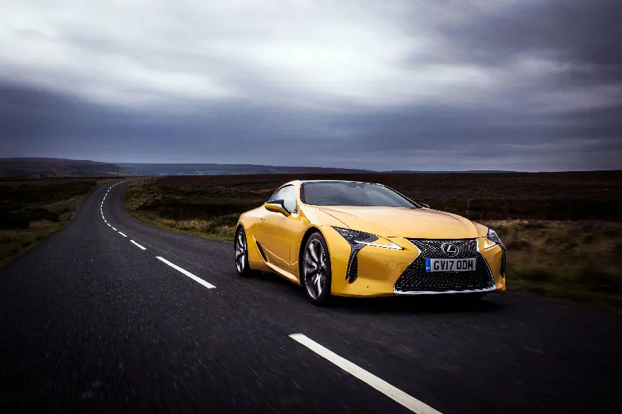 تصویر استوک لکسوس LC 500 زرد خوش رنگ در جادە‌ای با آسمان ابری تیرە