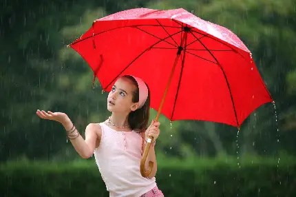 تصویر دختربچە زیبا با لباس صورتی رنگ با چتر قرمز رنگ در باران واقعی باکیفیت اچ دی