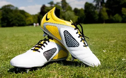 تصویر زمینه تماشایی از کفش ورزشی زیبا به رنگ زرد و سفید در زمین چمن