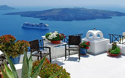بک گراند از فضای شاداب با گل‌های قشنگ و میز و صندلی در ساحل جزیره سانتورینی