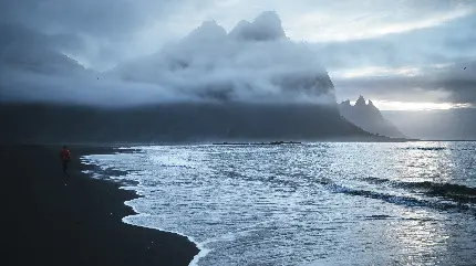 عکس زمینە سیاە و سفید خاص گوشی از نمای کنار اقیانوس با ابرهای پراکندە و کوه نامعلوم