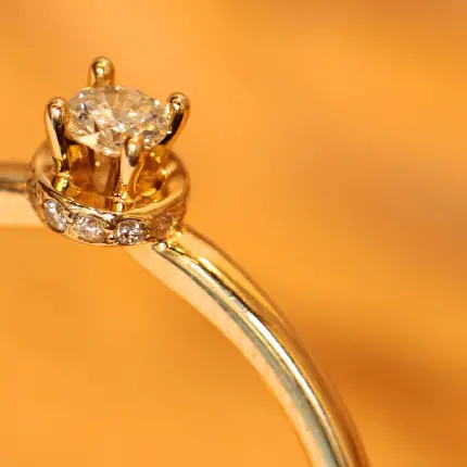 عکس نصفە نیمە از انگشتر الماس طلایی در زمینە نارنجی رنگ