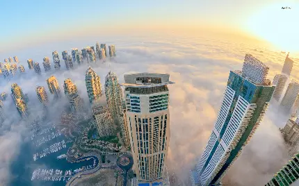 تصویر زمینە جالب توجە از ساختمان‌های بلند شهر کە از میان ابرهای سفید گذشتە‌اند