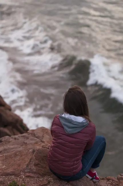 تصویر زمینه استثنایی از دختر بالای صخره در حال تماشای دریای خروشان 