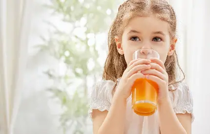 پس زمینه زیبا از دختر بچه ناز در حال نوشیدن نوشیدنی نارنجی رنگ