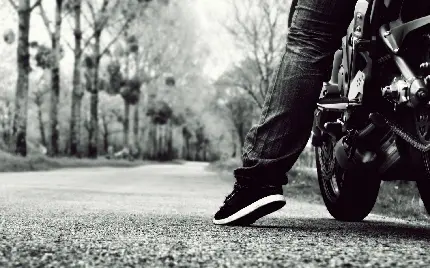 عکس زمینە سیاە و سفید تازە از یک پای رانندە موتور سیکلت سیاە رنگ در جادە جنگلی