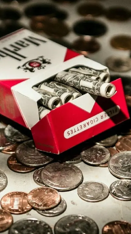 تصویر فانتزی تجملی از نخ‌های پیچیدە شدە دلار در جعبە سیگار مارلبرو و سکە‌های بیشمار در اطرافش