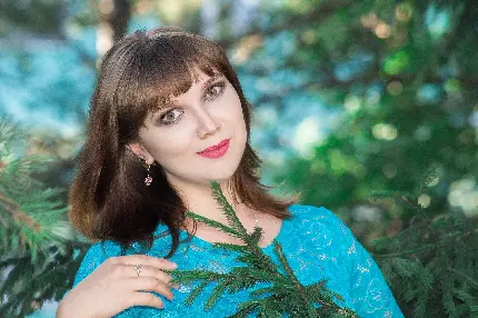والپیپر خوش رنگ از دختر ناز با چشم و مو قهوەای و لباس آبی رنگ توری در کنار برگ‌های سبز رنگ