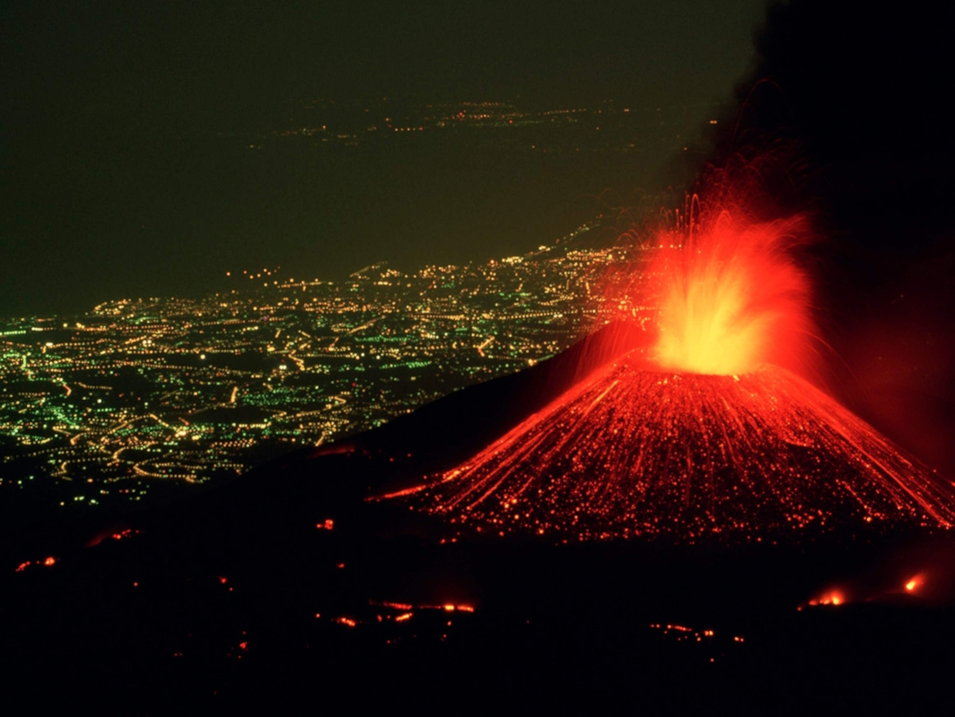 چشم انداز شهر در شب از فوران کوه آتشفشان فعال نارنجی رنگ 
