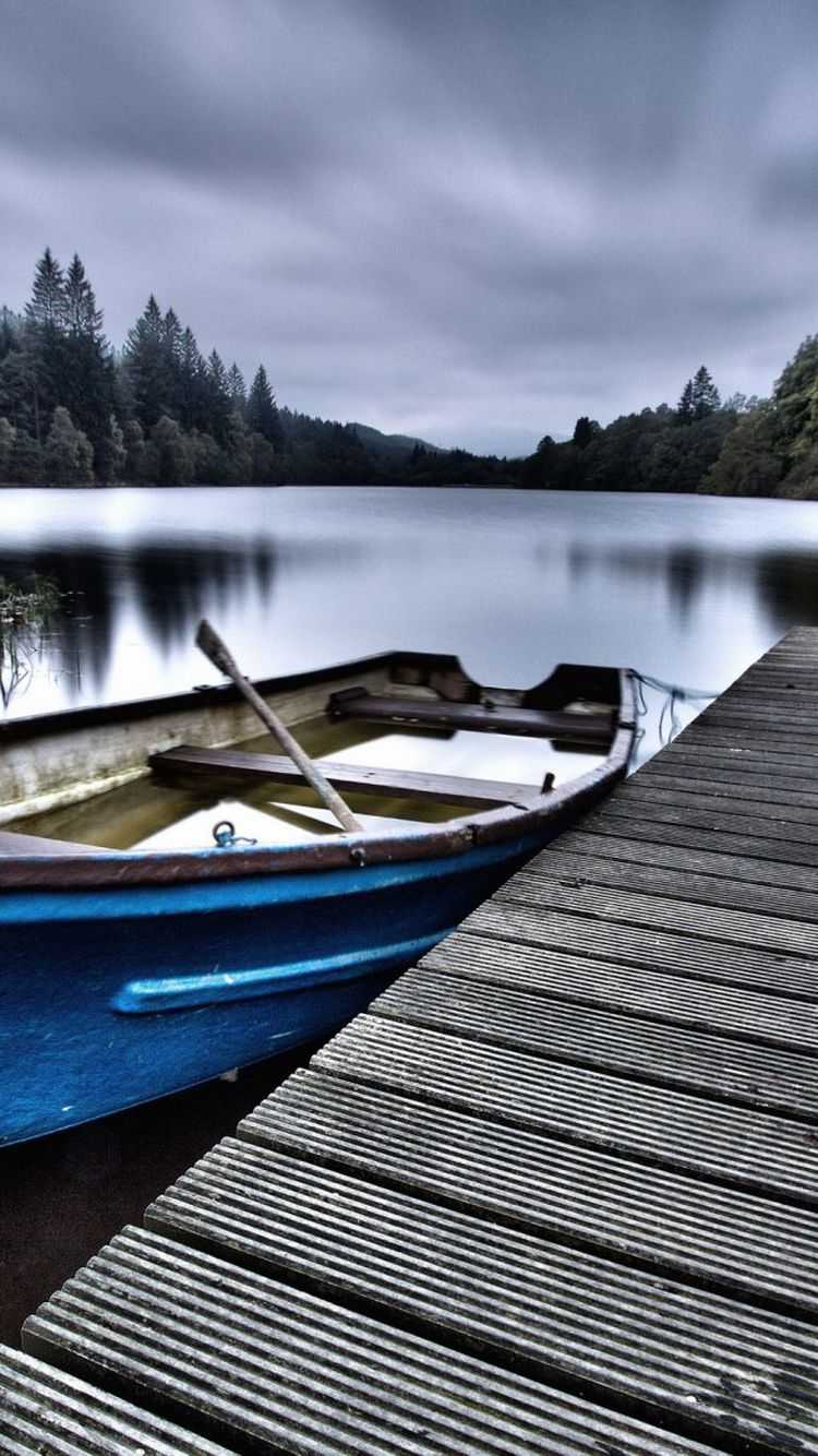عکس قایق چوبی تنها کنار دریاچه زیر هوای ابری برای زمینه گوشی