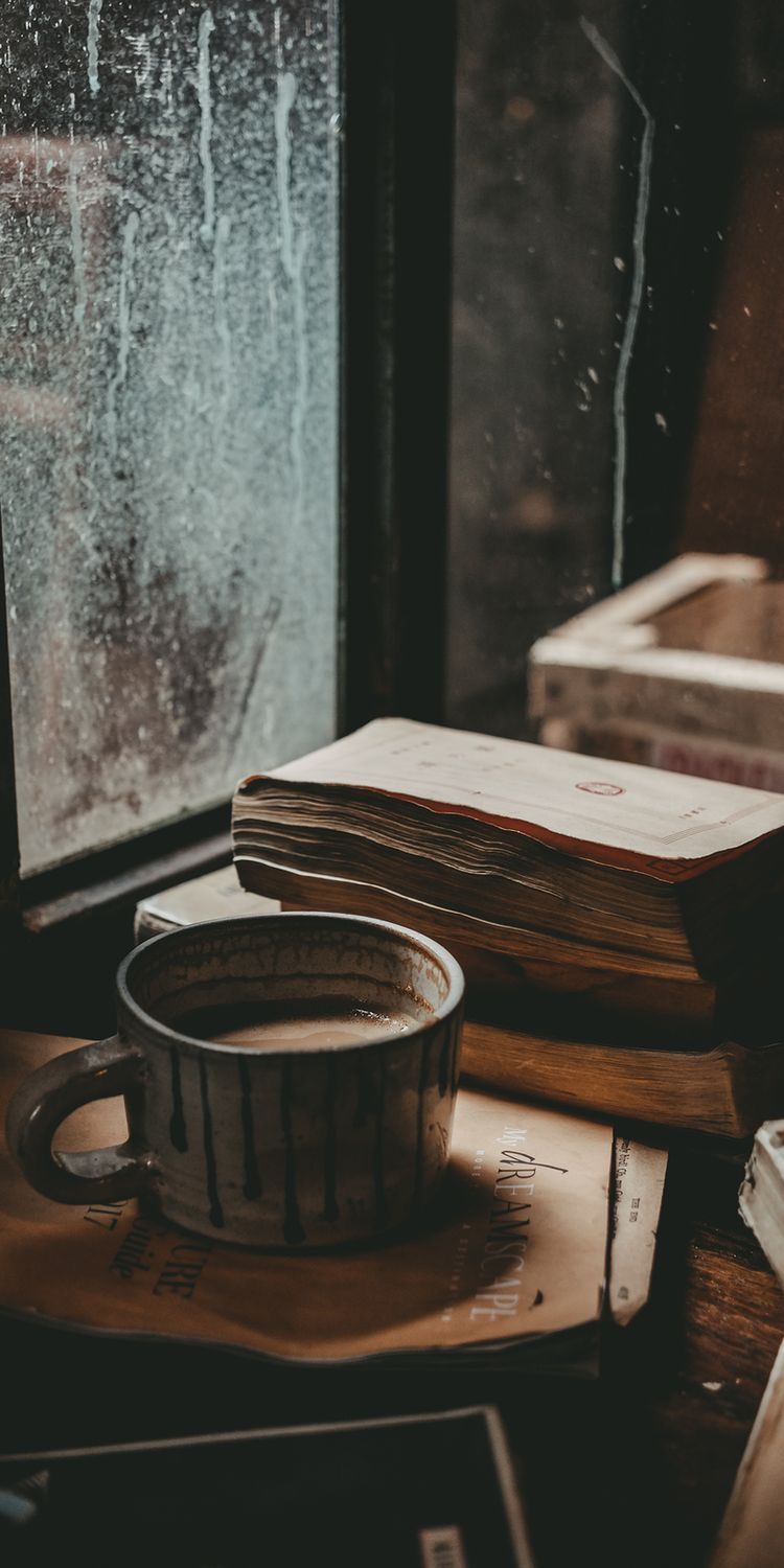 پروفایل غمگین فنجان قهوه در کنار کتاب و پنجره باران زده