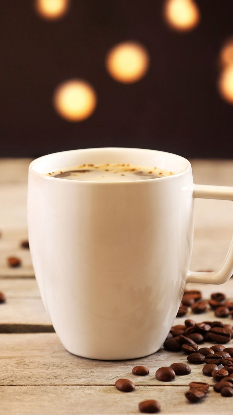 تصویر لیوان سفید قهوه از پهلو نزدیک دانه های طبیعی قهوه