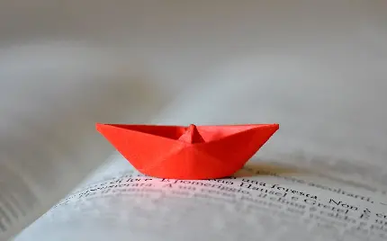 تصویر زمینه مینیمال قایق کاغذی قرمز کوچک روی صفحات کتاب