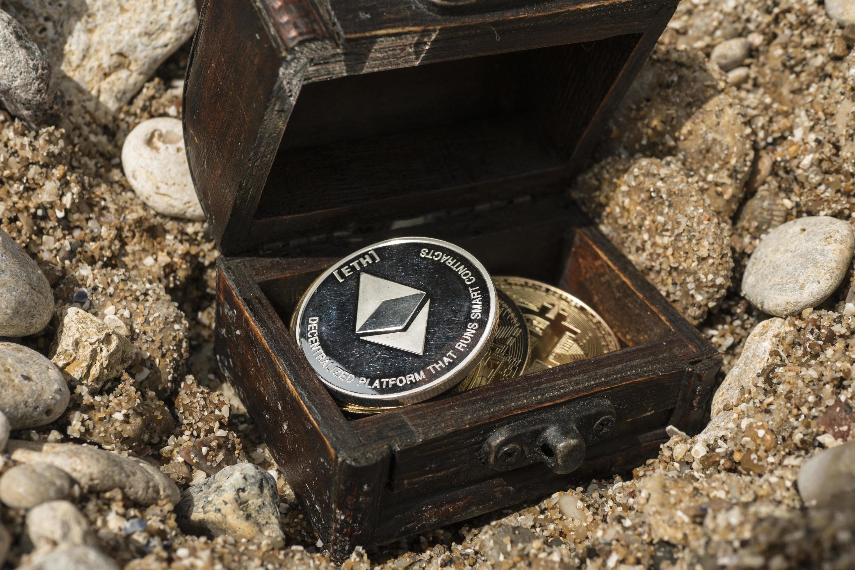 عکس صندوقچه کوچک چوبی با سکه های مختلف روی شنزار ساحلی