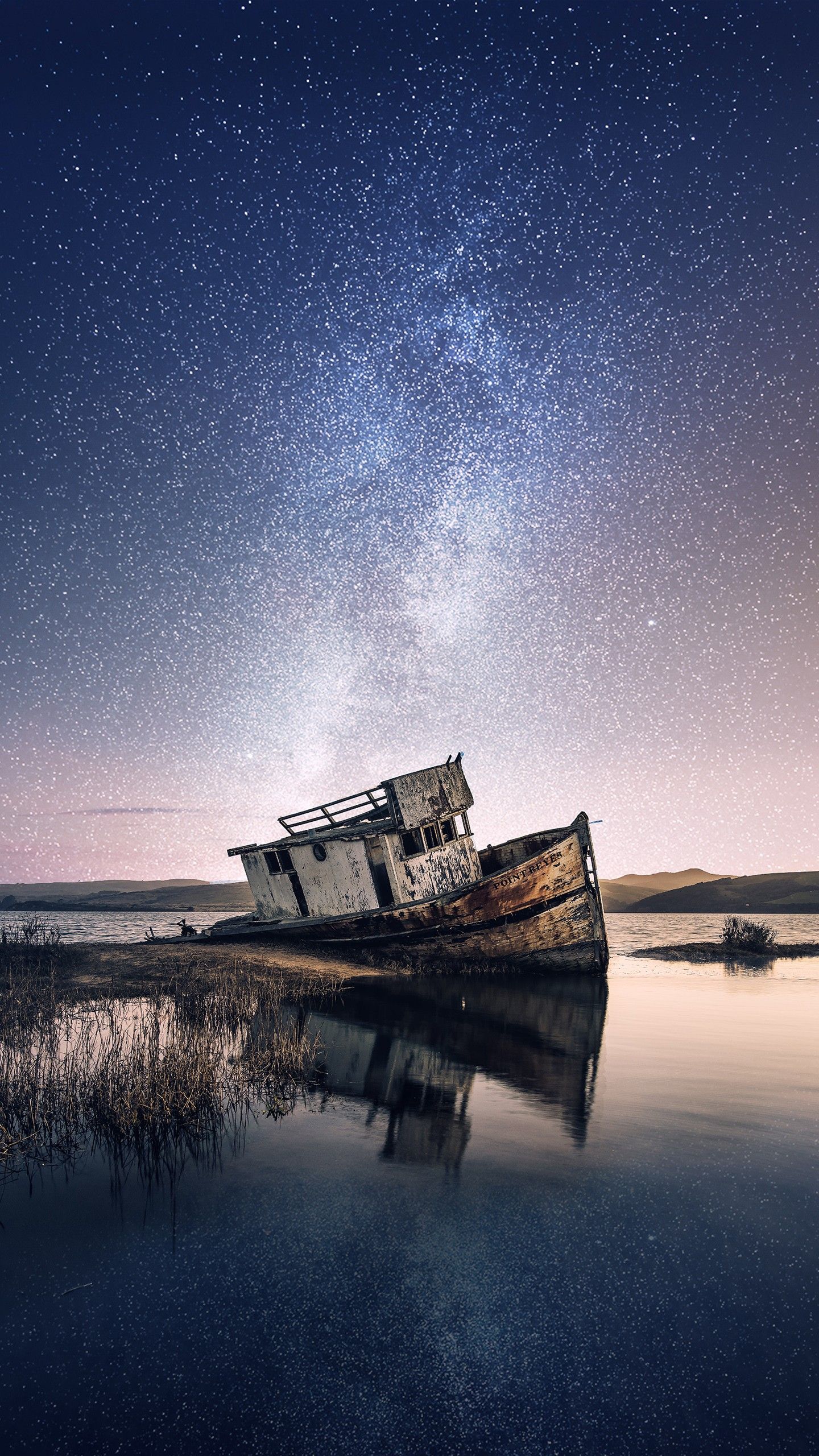 عکس قایق قدیمی گردشگری رها شده کنار ساحل زیر آسمان پرستاره شب