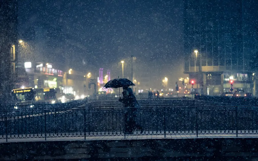 دانلود عکس رایگان دختر با چتر برفی نشسته روی نیمکت با والپیپر چشم انداز شهری 