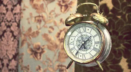 عکس ساعت قدیمی رومیزی با پس زمینه مات کاغذ دیواری گلدار