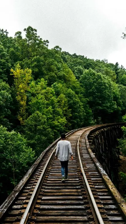 عکس مرد تنها در حال دویدن روی ریل راه آهن در کنار درختان 