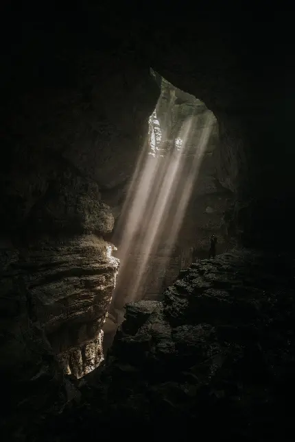 عکس زمینه غار تاریک زیر زمین با روزنه های نور از سطح زمین 