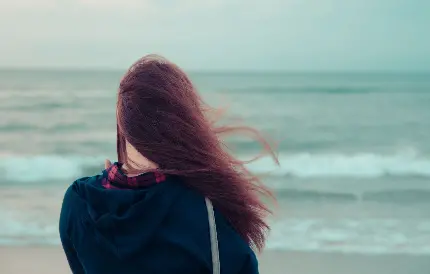 دختر غمگین و تنها کنار دریا با موهای باز خرمایی