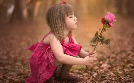دختر بچه ناز و شیرین با یک شاخه گل رز صورتی در دست