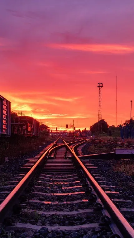 ریل قطار با چشم انداز آسمان سرخ و طلایی غروب برای مسافرت