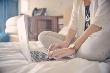 نویسنده زن در حال تایپ کردن با لپ تاپ روی تخت خواب