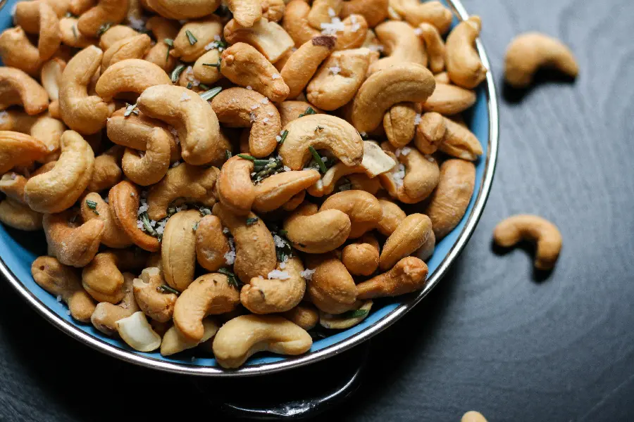 بادام هندی و نمک در کاسه ای آبی رنگ روی تخته چوب مشکی