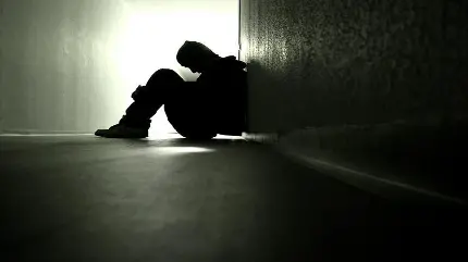 پسر غمگین و تنها کنج اتاق و زانو در بغل حالت گریه و تنها