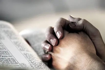 دست های دعا کننده در کنار کتاب مقدس