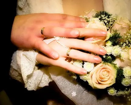 تصویر دست‌های عروس و داماد کنار دست گل